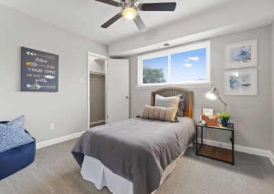 A cozy twin bedroom featuring a ceiling fan above a neatly made bed and side table