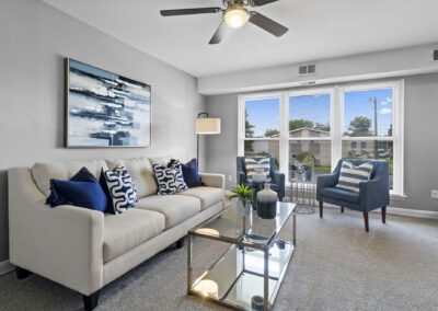 A cozy living room featuring a ceiling fan and stylish blue and white furniture and a glass table with vases